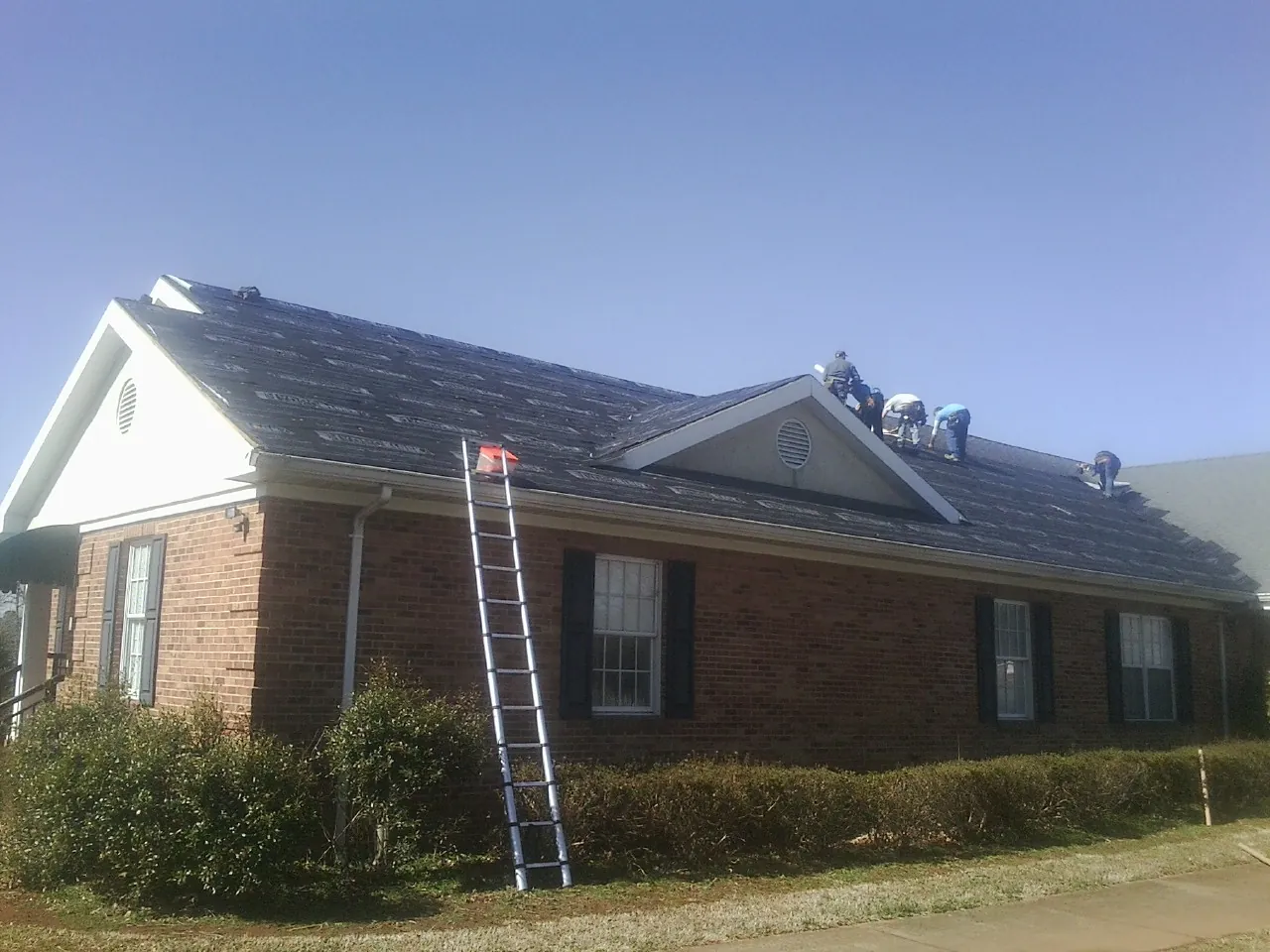 Crew tearing shingles off a brick ranch roof with a ladder set — Metal Roof Repair work by our crew in Mansfield