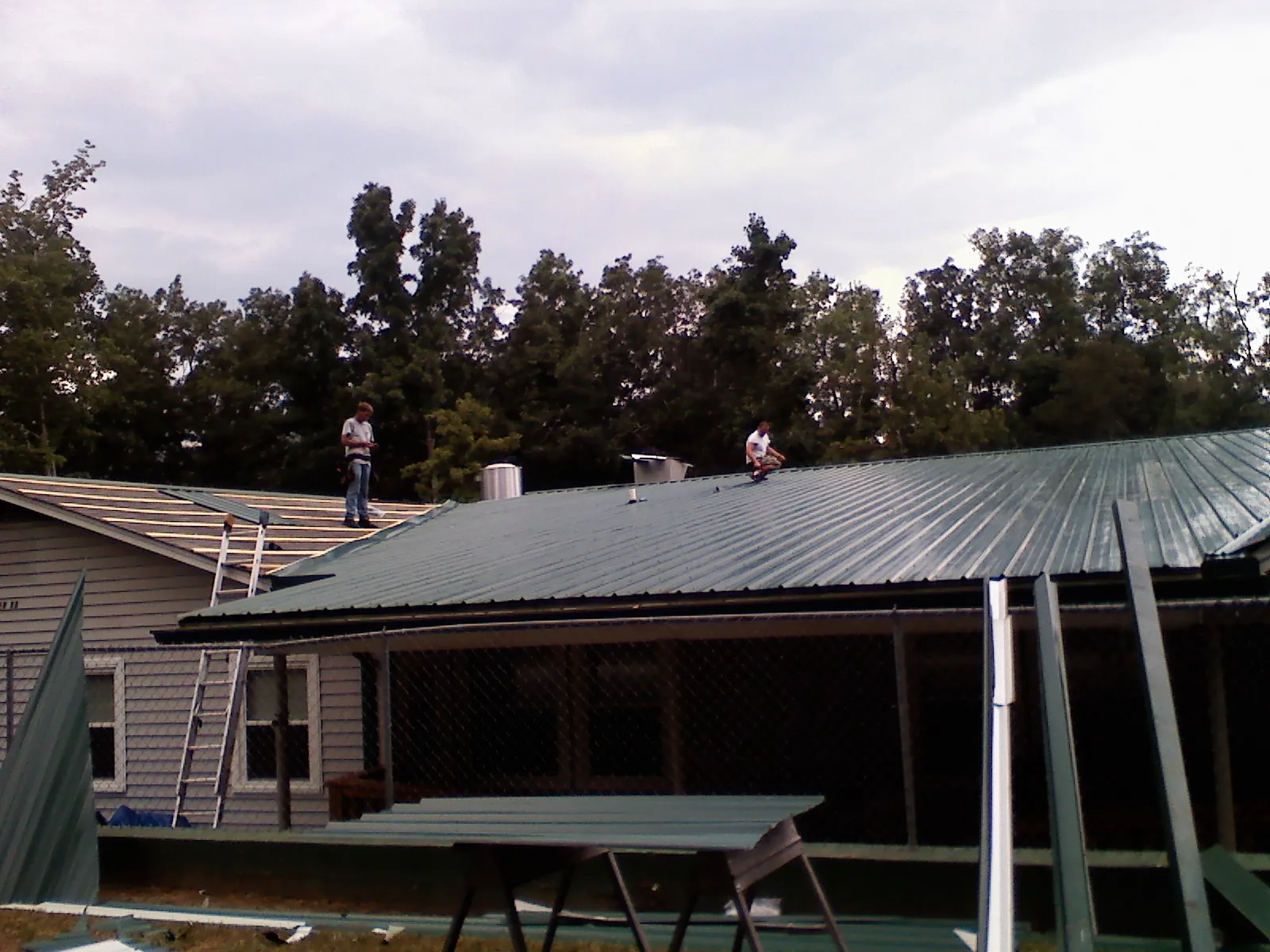 Two roofers installing green metal panels above a covered porch in Mansfield