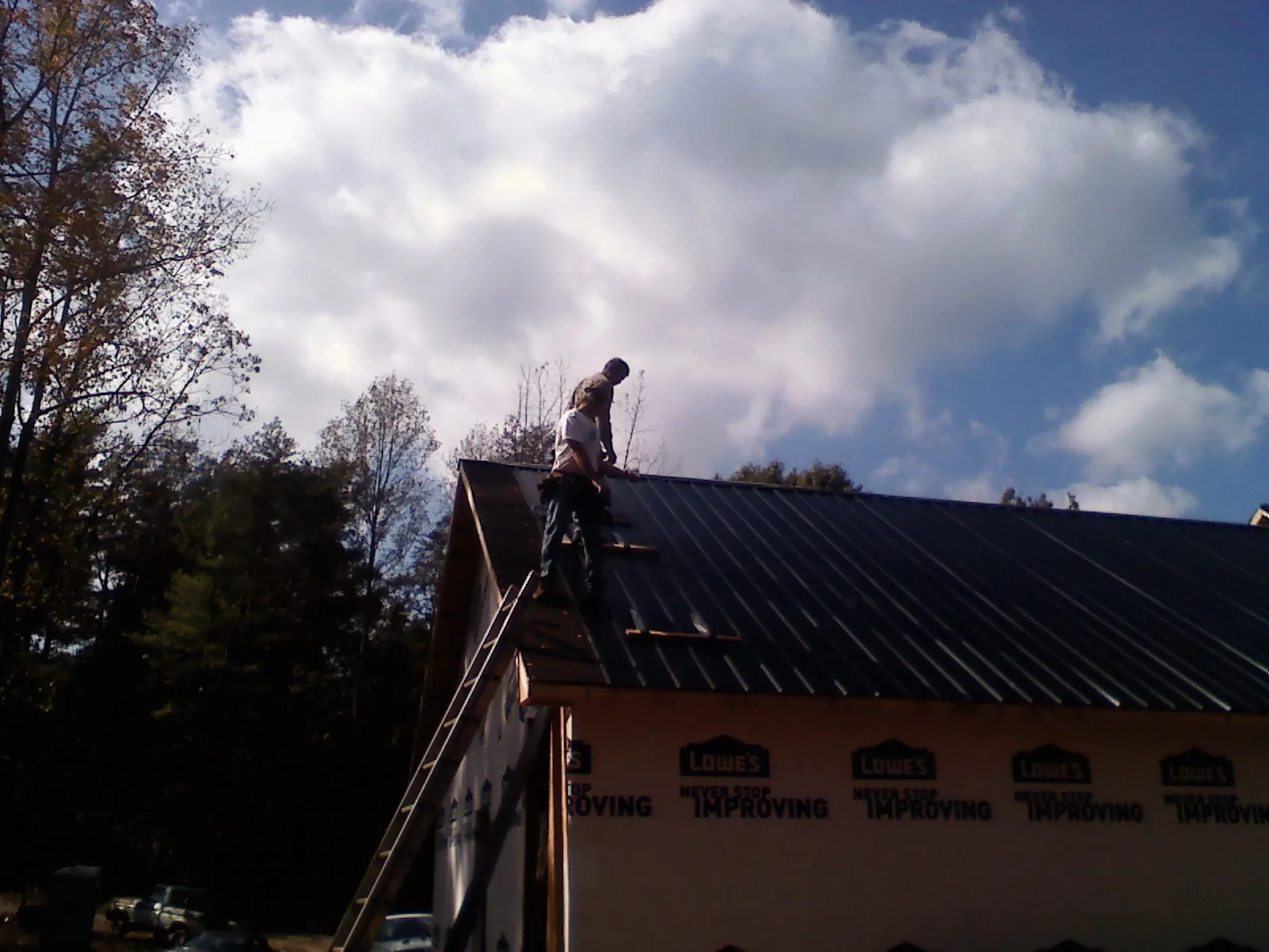 Roofer fastening dark metal panels high against a cloudy sky, from a Roof Inspection job in Mansfield